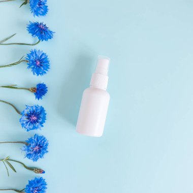 Üst görüntü ve yakın plan, markasız beyaz plastik sprey şişesi ve mavi arkaplanda mavi renkte çiçeklerden oluşan bir kenar. Doğal organik spa kozmetik ürünleri ve sıvı antimikrobik sprey