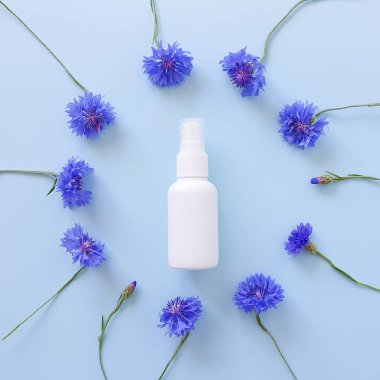 Üst manzara ve yakın plan, markasız beyaz plastik sprey şişenin mavileşmesi ve mavi arka planda mavi renkli desenlerin çiçek çerçevesi. Doğal organik spa kozmetik ürünleri ve sıvı antimikrobik sprey.