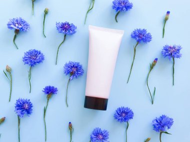 Mavi arka planda siyah başlık ve mavi çiçek desenli pembe sıkma şişe plastik tüpünün üst görüntüsü. Doğal organik spa kozmetik konsepti. Düz Yatay