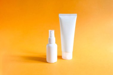 Kalıplı parlak turuncu arka planda damgalamak ve etiketlemek için iki markasız beyaz şişenin maketleri. Bunlardan biri sıkılmış plastik tüp. Diğeri plastik sprey şişesi. Doğal organik spa