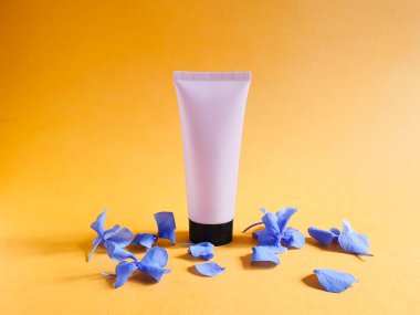 Pembe sıkılmış plastik tüp, siyah kapaklı ve parlak turuncu arka planda mavi ortanca çiçekleri. Damgalamak ve etiketlemek için bir şişe. Doğal organik kaplıca ürünleri