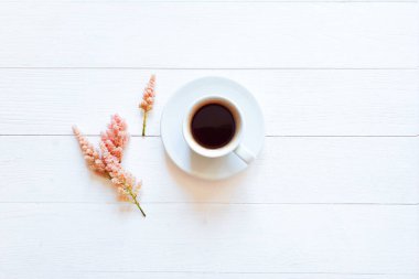 Bir fincan kahve, sıcak çikolata ve beyaz ahşap arka planda küçük pembe çiçekler. Düz yaşam biçimi, kopyalama alanı, modelleme.