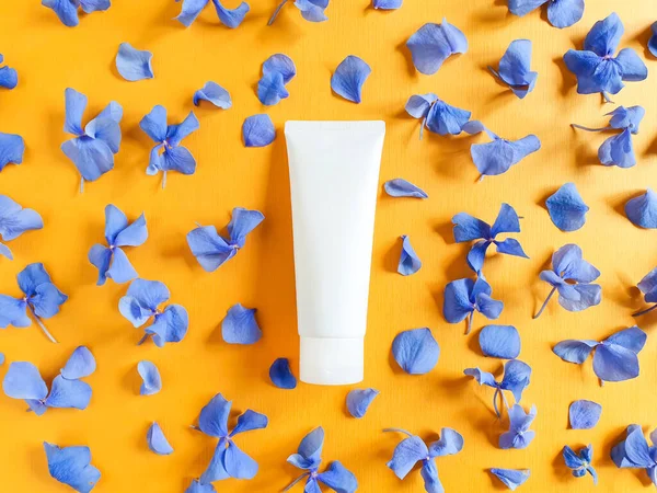Mock-up bottle for branding and label.  Top view of petals of blue hydrangea flowers and mockup of white squeeze bottle plastic tube on a textured bright orange background. Natural organic cosmetics