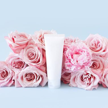 Damgalamak ve etiketlemek için markasız beyaz şişe ve pastel mavi arka planda açık pembe güller. Plastik tüpü sık. Doğal organik spa kozmetik konsepti. Kare fotoğrafçılık.