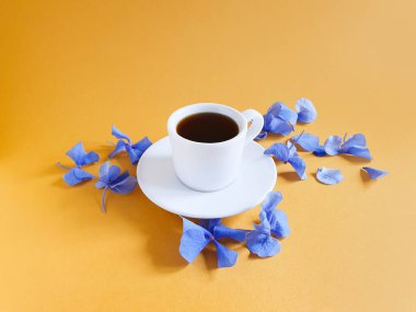 Bir fincan kahve / sıcak çikolata ve parlak sarı turuncu arka planda mavi ortanca çiçekleri. Uzayı kopyala, model. Aroma ve günaydın konsepti.
