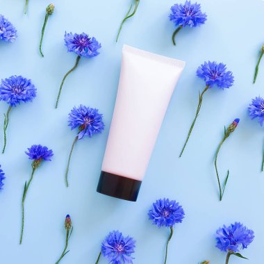 Açık pembe sıkılmış plastik tüp, siyah kapaklı ve mavi çiçekli. Üst düzey, Flatlay yaşam tarzı. Doğal organik spa kozmetik konsepti. Kare fotoğraf.