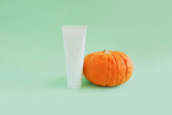 Boş beyaz sıkma şişe plastik tüp ve yeşil arka planda parlak balkabağı. Temiz güzellik konsepti.