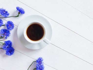 Kahve fincanının üst görüntüsü, parlak mavi çiçekler beyaz ahşap bir arka planda. Çiçekli düzlük. Günaydın konsept..