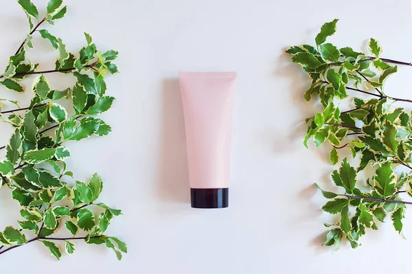 Mock-up of pink squeeze bottle plastic tube with black cap and fresh greens on white background. Bottle for branding and label. Natural organic spa cosmetics concept. Top view, flatlay