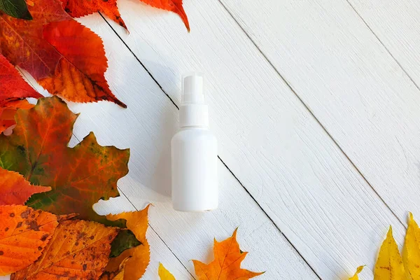 Mock-up of white plastic spray bottle and autumn bright colorful leaves on a white wooden table. Top view, mock-up, flatlay.