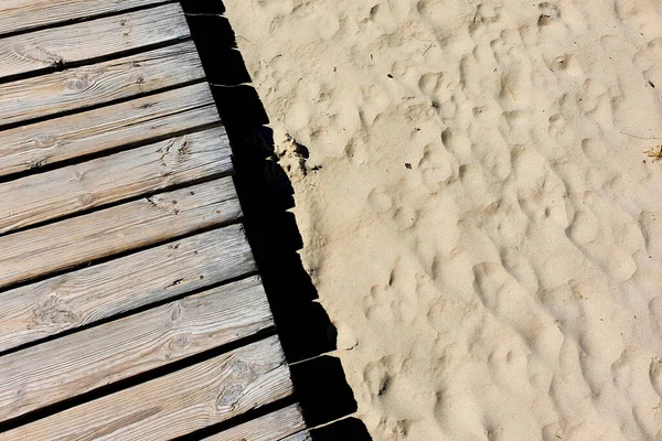 Wooden walkway on the sandy beach. Wooden boardwalk and light soft sand. Top view.