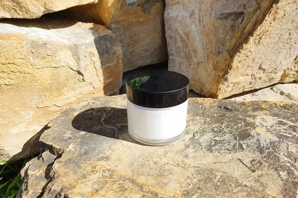 Moisturizer facial or eye cream in white glass jar with black cup on a stone / rock background. Concept eco natural organic skincare and bodycare beauty product. Mockup