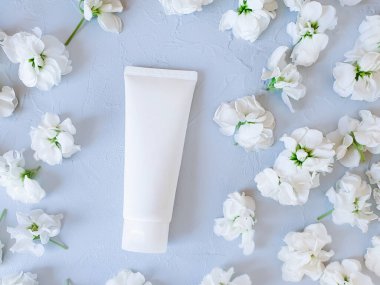 Beyaz sıkılmış plastik tüp ve açık gri arka planda küçük beyaz çiçekler. Doğal organik kozmetik kavramı. Model, üst görünüm.