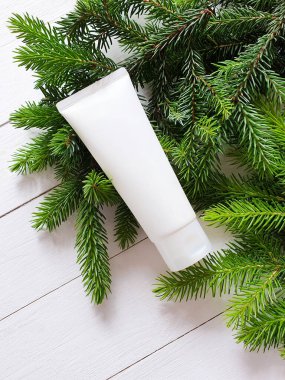 Beyaz sıkılmış kozmetik tüpü ve beyaz ahşap masada Noel ağacı dalları. Üst Manzara. Doğal organik kozmetik konsepti