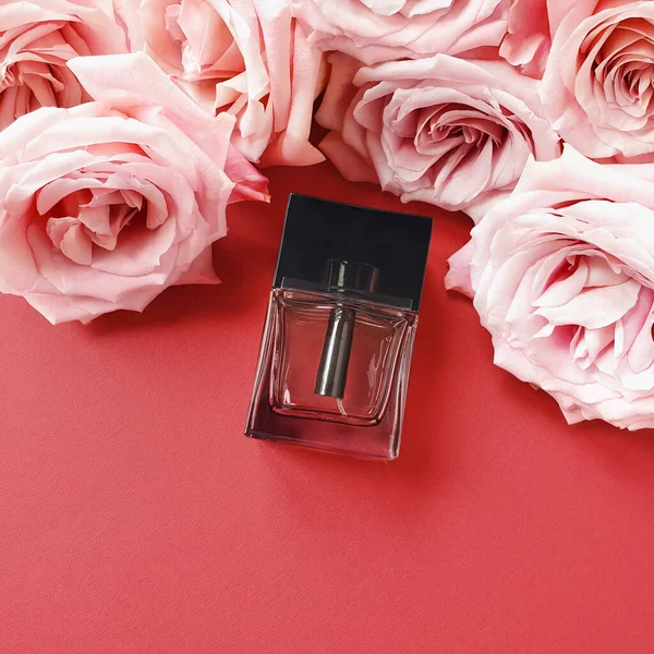Rectangular transparent black glass perfume bottle and pink flowers on red table. Top view. Eau de toilette. Mockup, copy space, flat lay style.