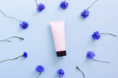 Mavi masanın üzerinde siyah kapaklı ve mavi çiçek çerçeveli pembe sıkılmış kozmetik tüp. Üst görünüm