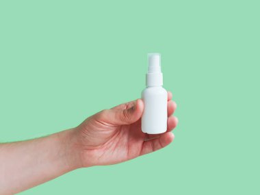 Marka, etiket ve yeşil arka planda erkek eli için markasız beyaz plastik sprey şişesinin maketi. Sıvı antimikrobik sprey konsepti. Minimalizm.