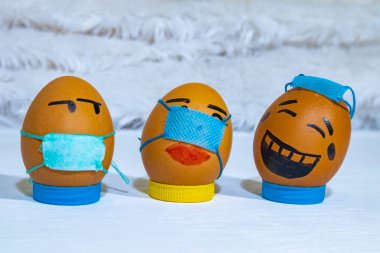 Birkaç tane boyanmış yumurta. Biri düzgün bir maske takıyor, biri uygun değil, diğeri maske takmıyor. Covid-19 illüstrasyon. Çocuklarla eğlenceli aktiviteler.