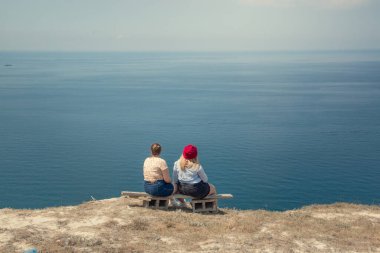İki arkadaş bir bankta oturuyor. Bir uçurumun kenarında inanılmaz bir deniz manzarası ve gökyüzünün arka planında rüzgarda dalgalanan saçlar. Arkadan manzara. Özgürlük kavramı