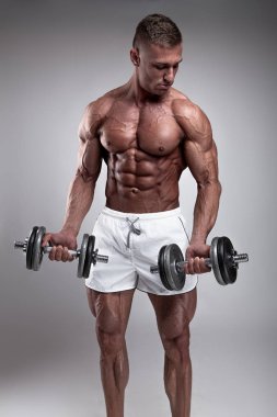 Gri arka plan üzerinde halter alıştırmalar yapan kaslı vücut geliştirmeci adam