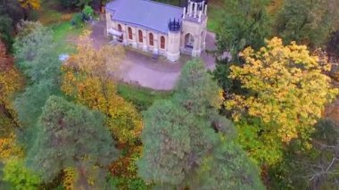 Ağaçların üzerinde uçmak ve sonbahar ormanındaki bir açıklıkta duran küçük, güzel bir gotik kilise.