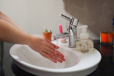 Açık tenli Asyalı kadın lavaboda ellerini duruluyor. Virüs ya da bakteriyel yayılma önleme için hijyen ve temizliği gösterir