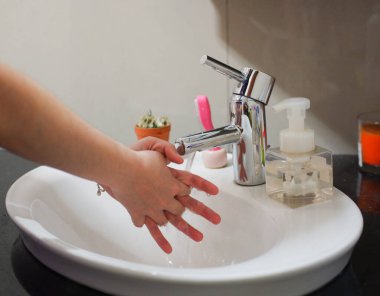 Açık tenli Asyalı kadın lavaboda ellerini duruluyor. Virüs ya da bakteriyel yayılma önleme için hijyen ve temizliği gösterir