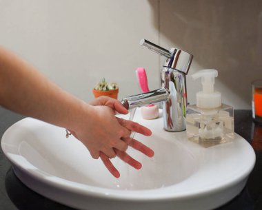 Açık tenli Asyalı kadın lavaboda ellerini duruluyor. Virüs ya da bakteriyel yayılma önleme için hijyen ve temizliği gösterir