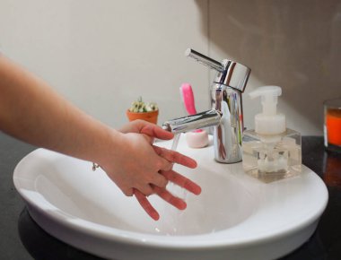 Açık tenli Asyalı kadın lavaboda ellerini duruluyor. Virüs ya da bakteriyel yayılma önleme için hijyen ve temizliği gösterir