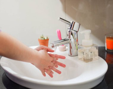 Açık tenli Asyalı kadın lavaboda ellerini duruluyor. Virüs ya da bakteriyel yayılma önleme için hijyen ve temizliği gösterir