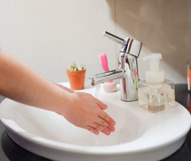 Açık tenli Asyalı kadın lavaboda ellerini duruluyor. Virüs ya da bakteriyel yayılma önleme için hijyen ve temizliği gösterir
