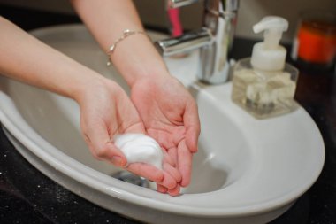 Açık tenli Asyalı kadın banyo lavabosunda el köpüğü sabunu gösteriyor. Virüs ya da bakteriyel yayılma önleme için hijyen ve temizliği gösterir