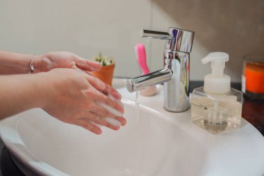 Açık tenli Asyalı kadın banyo lavabosunda köpüklü ellerini sabunla yıkıyor. Virüs ya da bakteriyel yayılma önleme için hijyen ve temizliği gösterir