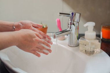 Açık tenli Asyalı kadın banyo lavabosunda köpüklü ellerini sabunla yıkıyor. Virüs ya da bakteriyel yayılma önleme için hijyen ve temizliği gösterir