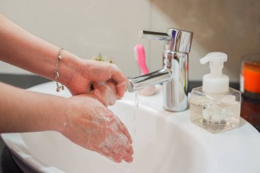 Açık tenli Asyalı kadın banyo lavabosunda köpüklü ellerini sabunla yıkıyor. Virüs ya da bakteriyel yayılma önleme için hijyen ve temizliği gösterir