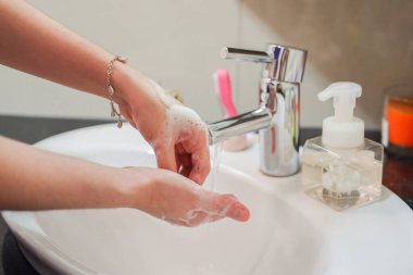 Açık tenli Asyalı kadın banyo lavabosunda köpüklü ellerini sabunla yıkıyor. Virüs ya da bakteriyel yayılma önleme için hijyen ve temizliği gösterir