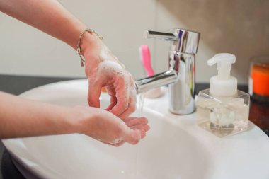 Açık tenli Asyalı kadın banyo lavabosunda köpüklü ellerini sabunla yıkıyor. Virüs ya da bakteriyel yayılma önleme için hijyen ve temizliği gösterir