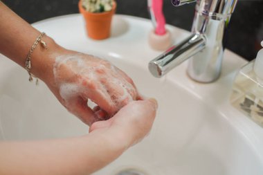 Açık tenli Asyalı kadın banyo lavabosunda köpüklü ellerini sabunla yıkıyor. Virüs ya da bakteriyel yayılma önleme için hijyen ve temizliği gösterir