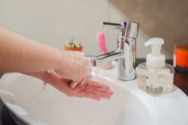 Açık tenli Asyalı kadın banyo lavabosunda köpüklü ellerini sabunla yıkıyor. Virüs ya da bakteriyel yayılma önleme için hijyen ve temizliği gösterir