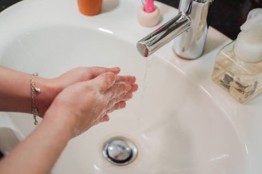 Açık tenli Asyalı kadın banyo lavabosunda köpüklü ellerini sabunla yıkıyor. Virüs ya da bakteriyel yayılma önleme için hijyen ve temizliği gösterir