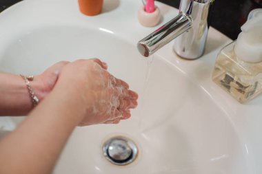 Açık tenli Asyalı kadın banyo lavabosunda köpüklü ellerini sabunla yıkıyor. Virüs ya da bakteriyel yayılma önleme için hijyen ve temizliği gösterir
