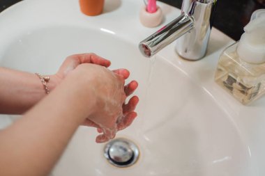 Açık tenli Asyalı kadın banyo lavabosunda köpüklü ellerini sabunla yıkıyor. Virüs ya da bakteriyel yayılma önleme için hijyen ve temizliği gösterir