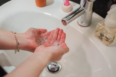 Açık tenli Asyalı kadın banyo lavabosunda köpüklü ellerini sabunla yıkıyor. Virüs ya da bakteriyel yayılma önleme için hijyen ve temizliği gösterir