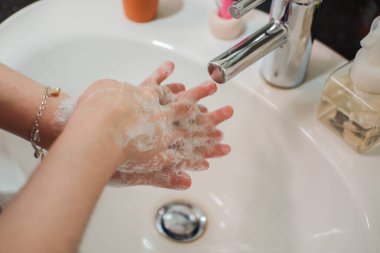 Açık tenli Asyalı kadın banyo lavabosunda köpüklü ellerini sabunla yıkıyor. Virüs ya da bakteriyel yayılma önleme için hijyen ve temizliği gösterir