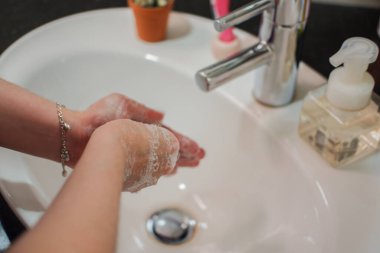 Açık tenli Asyalı kadın banyo lavabosunda köpüklü ellerini sabunla yıkıyor. Virüs ya da bakteriyel yayılma önleme için hijyen ve temizliği gösterir