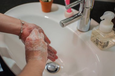 Açık tenli Asyalı kadın banyo lavabosunda köpüklü ellerini sabunla yıkıyor. Virüs ya da bakteriyel yayılma önleme için hijyen ve temizliği gösterir