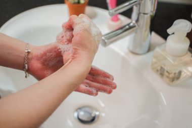 Açık tenli Asyalı kadın banyo lavabosunda köpüklü ellerini sabunla yıkıyor. Virüs ya da bakteriyel yayılma önleme için hijyen ve temizliği gösterir