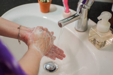 Açık tenli Asyalı kadın banyo lavabosunda köpüklü ellerini sabunla yıkıyor. Virüs ya da bakteriyel yayılma önleme için hijyen ve temizliği gösterir
