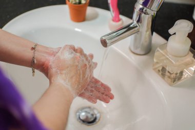 Açık tenli Asyalı kadın banyo lavabosunda köpüklü ellerini sabunla yıkıyor. Virüs ya da bakteriyel yayılma önleme için hijyen ve temizliği gösterir