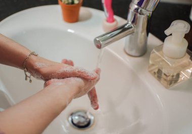 Açık tenli Asyalı kadın banyo lavabosunda köpüklü ellerini sabunla yıkıyor. Virüs ya da bakteriyel yayılma önleme için hijyen ve temizliği gösterir